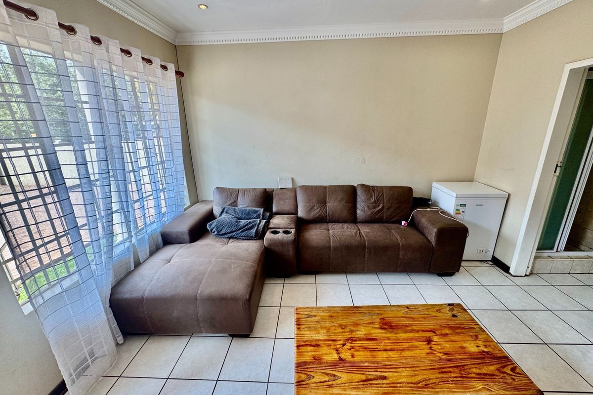 A living room featuring tiled flooring, decorative crown molding, and recessed lighting, providing a functional space with natural light from a large window.