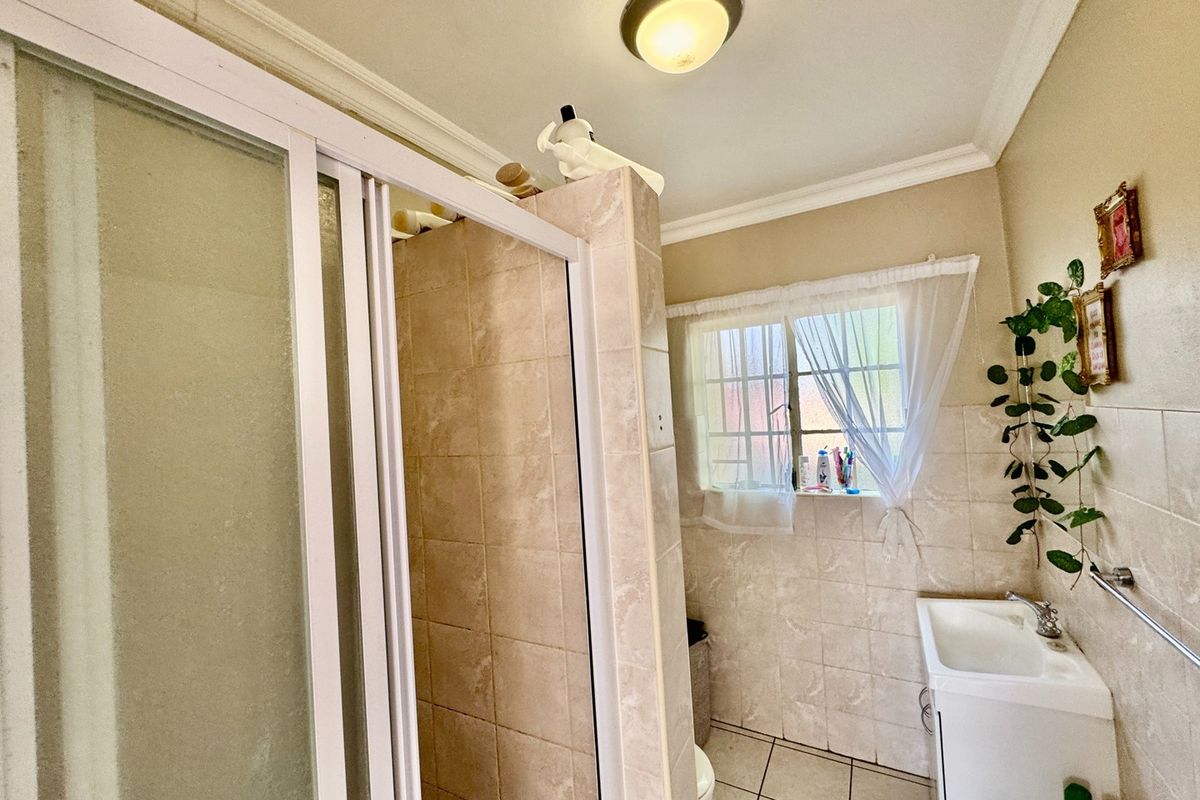 A functional bathroom featuring a shower enclosure, tiled walls and flooring, and a vanity basin with a window providing natural light.