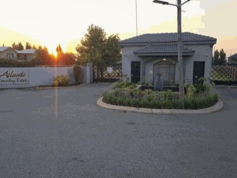 Entrance view of Ailanto Country Estate featuring a secure guard house, gated access, and a landscaped traffic island.