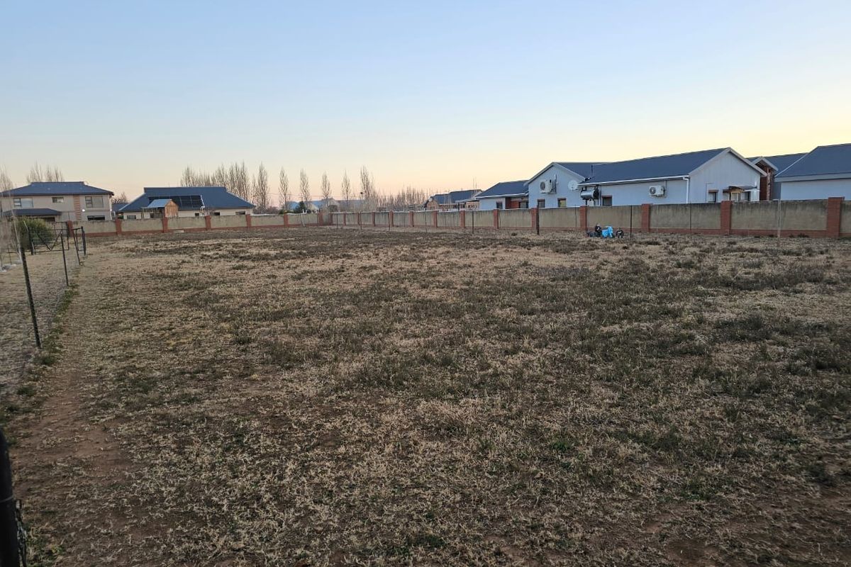 A vacant residential plot featuring a level grass area enclosed by a perimeter brick wall and wire fencing.