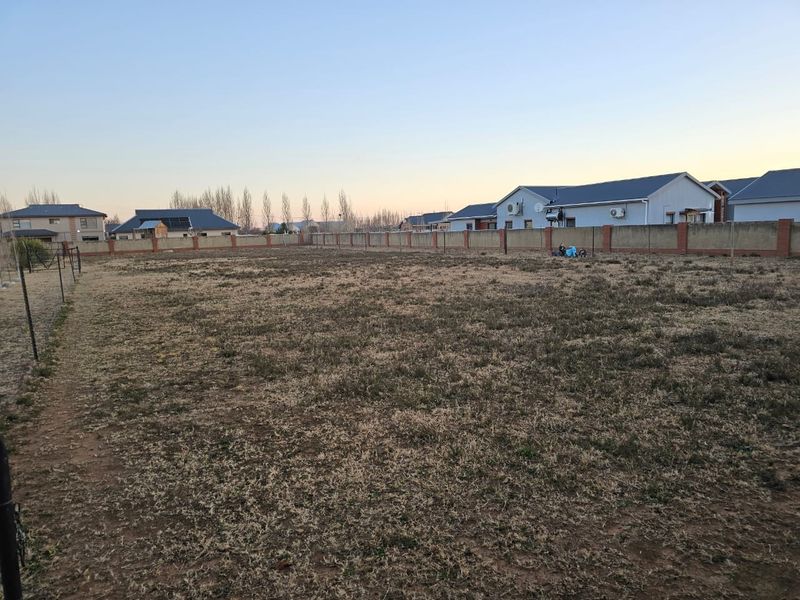 A vacant residential plot featuring a level grass area enclosed by a perimeter brick wall and wire fencing.