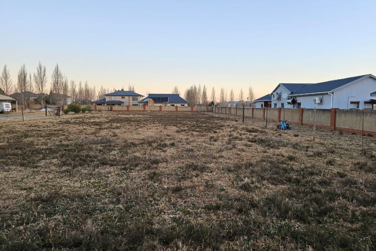 A vacant residential plot featuring a perimeter brick wall and fencing, situated in a developed neighborhood.