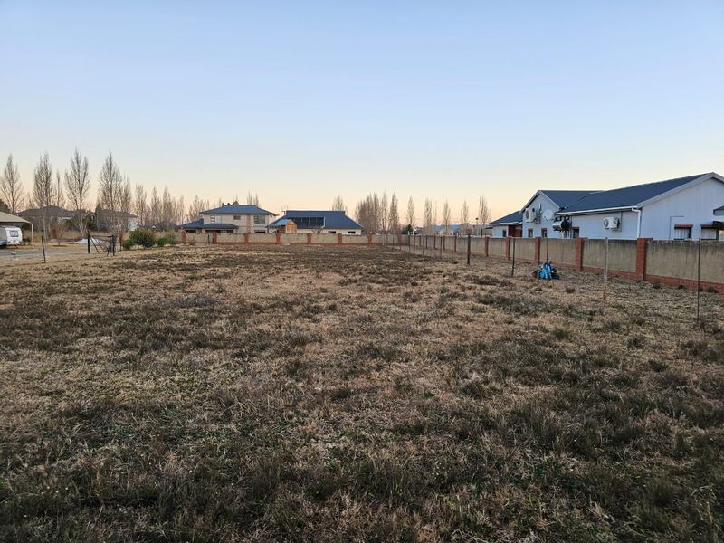 A vacant residential plot featuring a perimeter brick wall and fencing, situated in a developed neighborhood.