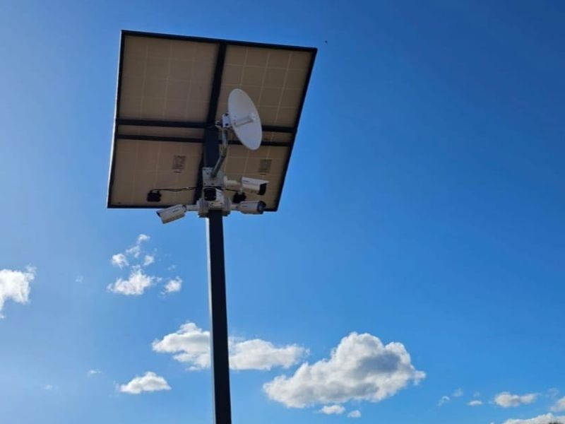 A utility pole equipped with solar panels, security cameras, and a satellite dish, providing infrastructure for site monitoring and power.
