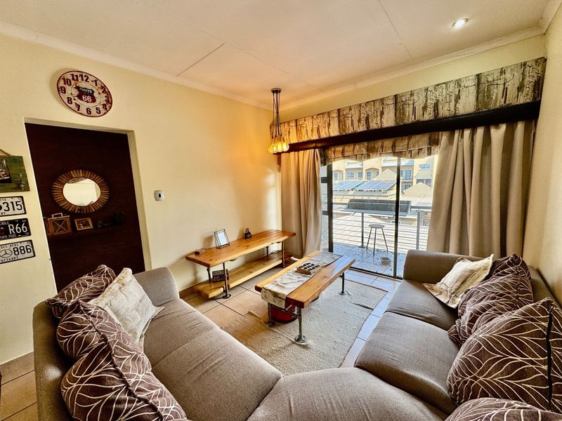 A comfortable living room featuring tiled flooring, recessed lighting, and a large sliding glass door providing access to an outdoor balcony area.