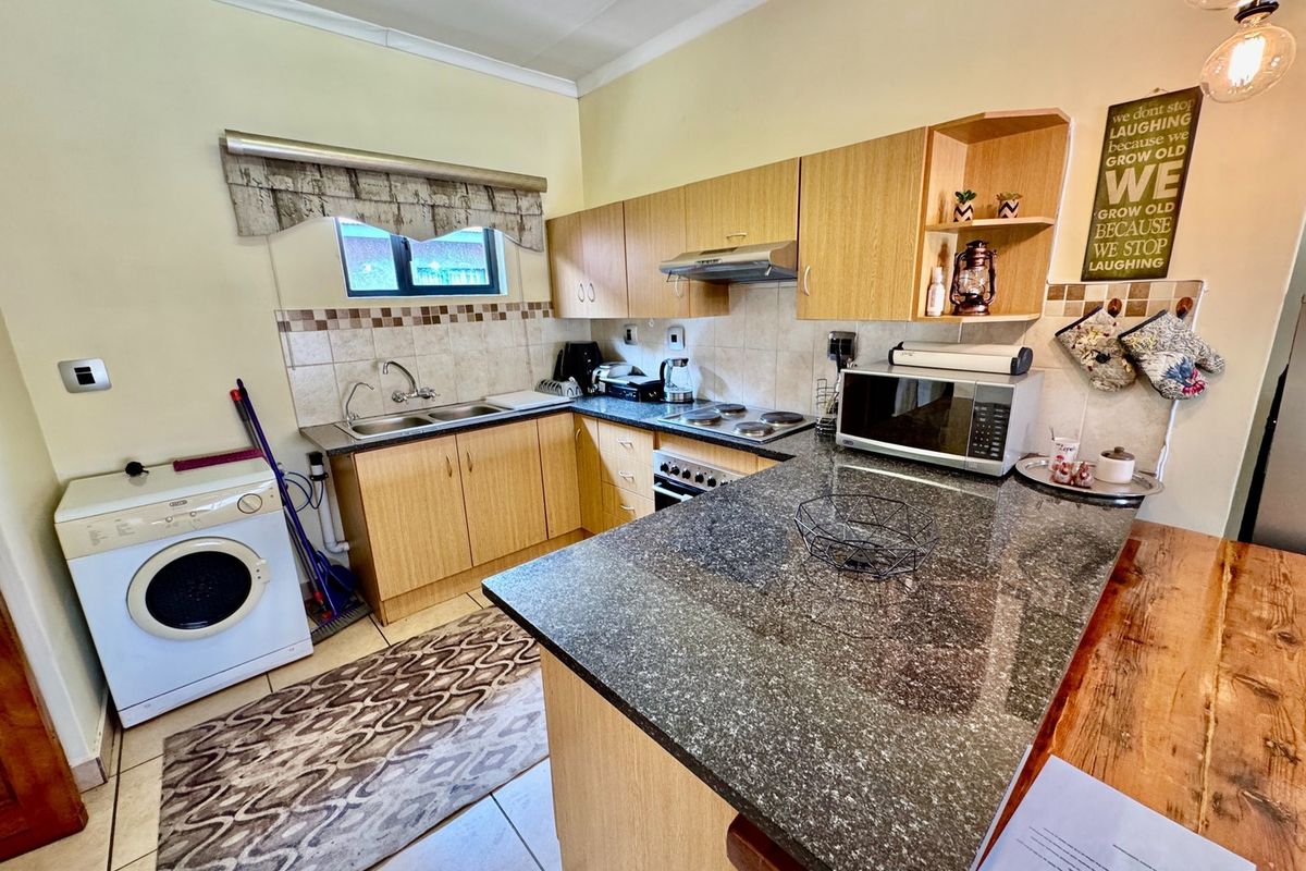 Functional kitchen featuring laminate cabinetry, granite countertops, built-in oven, electric hob, extractor fan, and tiled flooring with integrated laundry space.