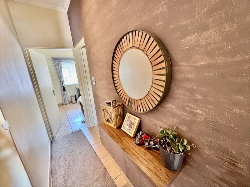 A hallway featuring a textured brown feature wall, a floating wooden shelf, and tiled flooring, leading into an adjacent bedroom.