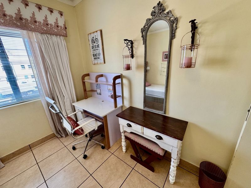A bedroom featuring tiled flooring and a window with blinds, currently utilized as a study area.