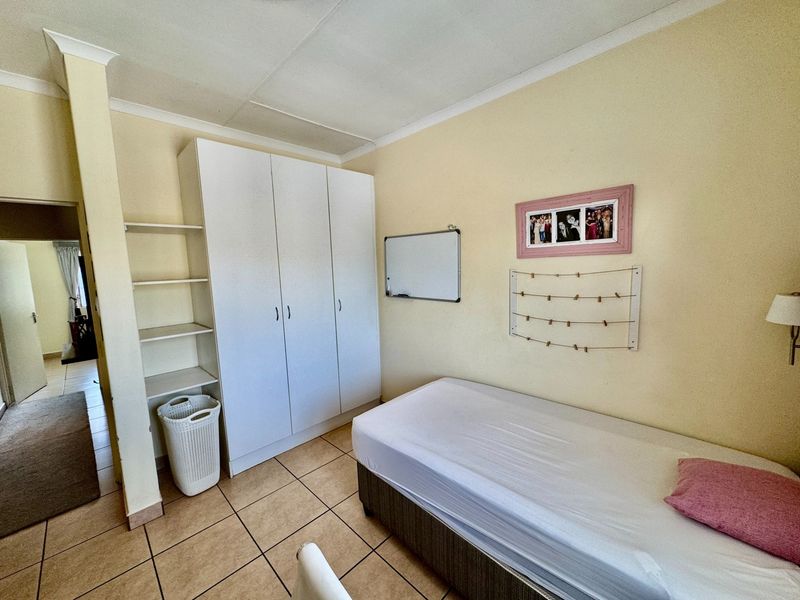 A functional bedroom featuring tiled flooring, a built-in wardrobe with integrated shelving, and coved ceiling details.