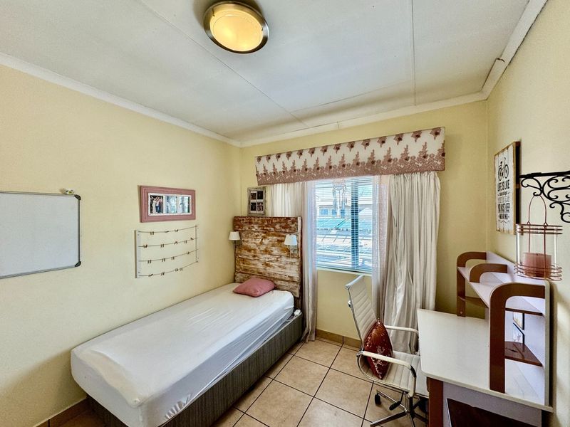 A functional bedroom featuring tiled flooring, a ceiling light fixture, and a window with fitted blinds, providing a comfortable living space.
