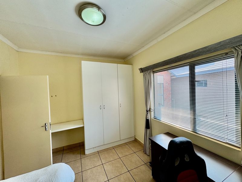 A functional bedroom featuring tiled flooring, a built-in wardrobe, and a built-in desk area with natural light from the window.