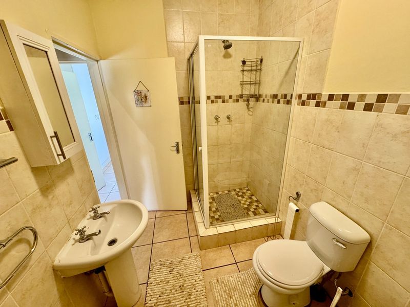 A functional bathroom featuring a pedestal sink, a glass-enclosed shower, and a standard toilet with neutral wall and floor tiling.