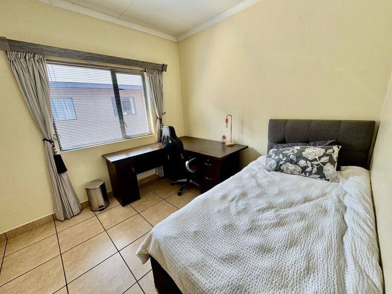 A functional bedroom featuring tiled flooring, a window with fitted blinds, and neutral wall finishes, providing a comfortable and practical living space.