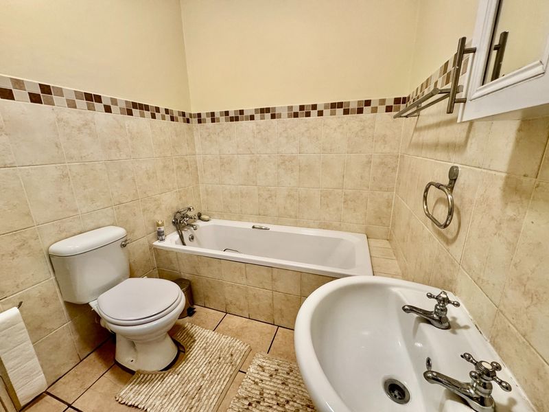 A functional bathroom featuring a bathtub, pedestal basin, and toilet with neutral tiled walls and flooring.