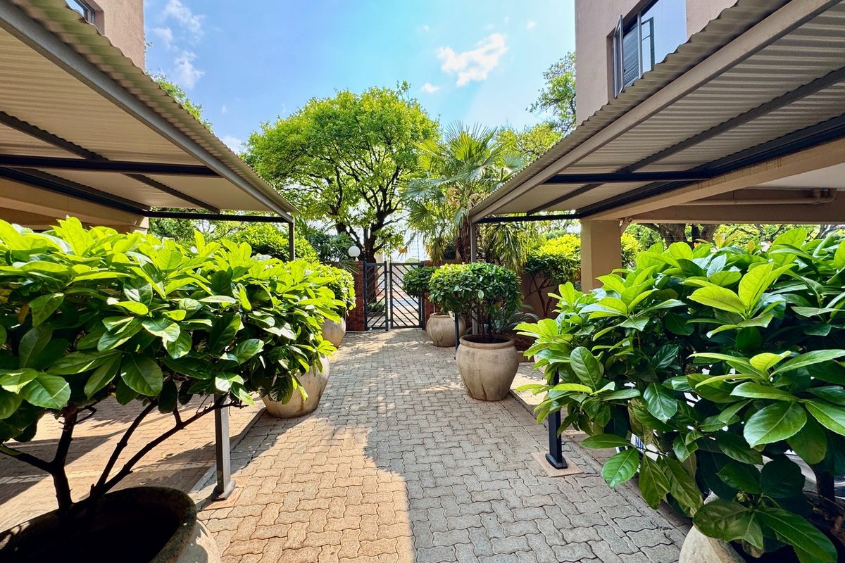 A well-maintained paved walkway between two building wings, featuring covered outdoor areas and a secure metal gate leading to the garden.