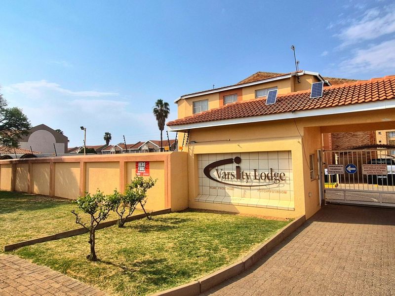 Front entrance view of Varsity Lodge featuring a secure gated access point, perimeter wall with electric fencing, and paved driveway.