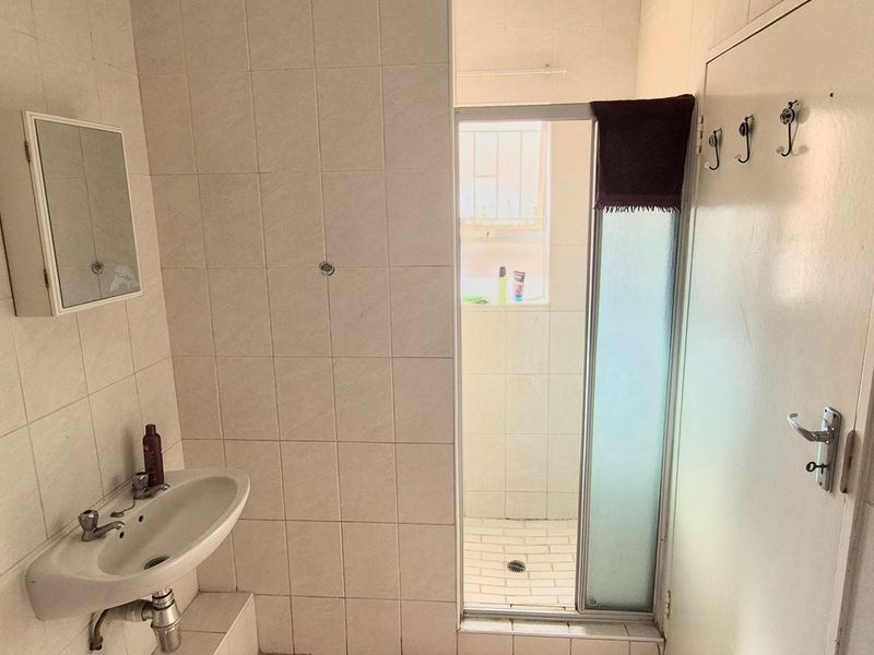 A functional bathroom featuring a wall-mounted basin, medicine cabinet, and a separate shower enclosure with tiled walls throughout.