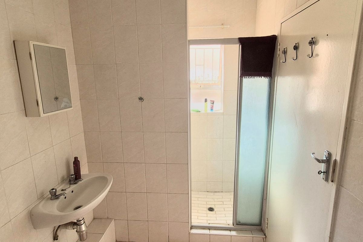 A functional bathroom featuring a wall-mounted basin, medicine cabinet, and a separate shower enclosure with tiled walls throughout.