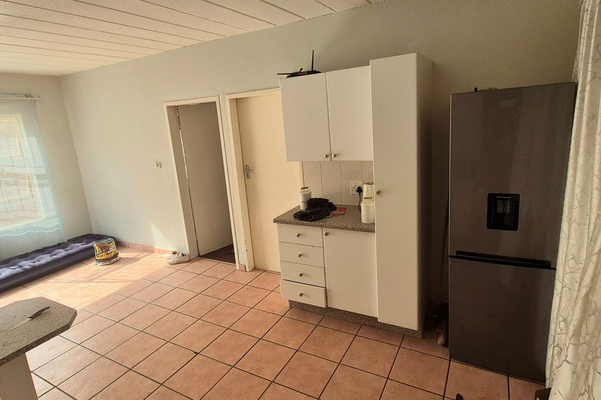 Open plan living area featuring tiled flooring, a compact kitchen unit with built-in cabinetry, and access to adjacent rooms.