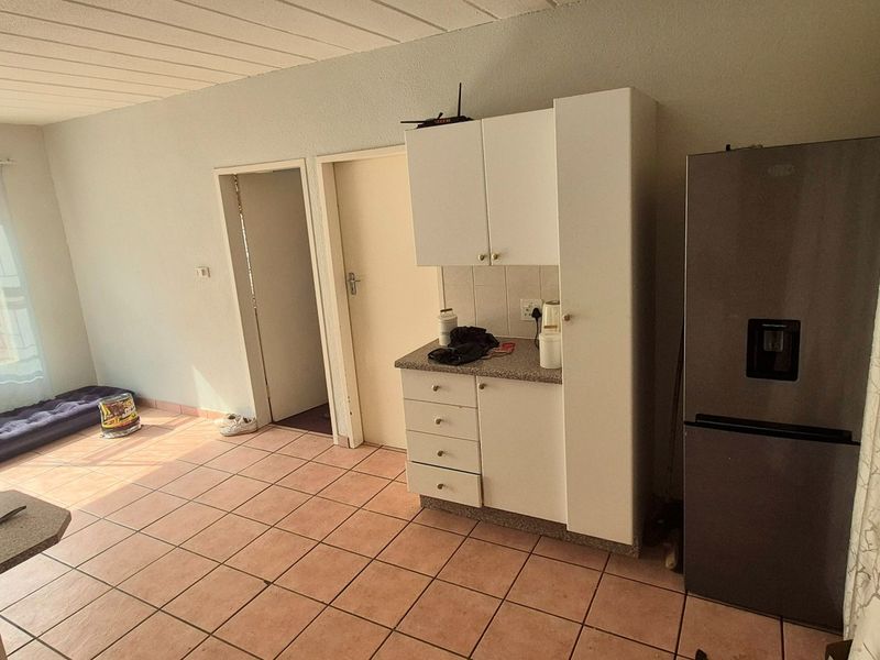 Open plan living area featuring tiled flooring, a compact kitchen unit with built-in cabinetry, and access to adjacent rooms.