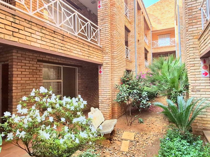 A view of the apartment complex courtyard featuring face brick architecture, tiled walkways, and established garden beds.