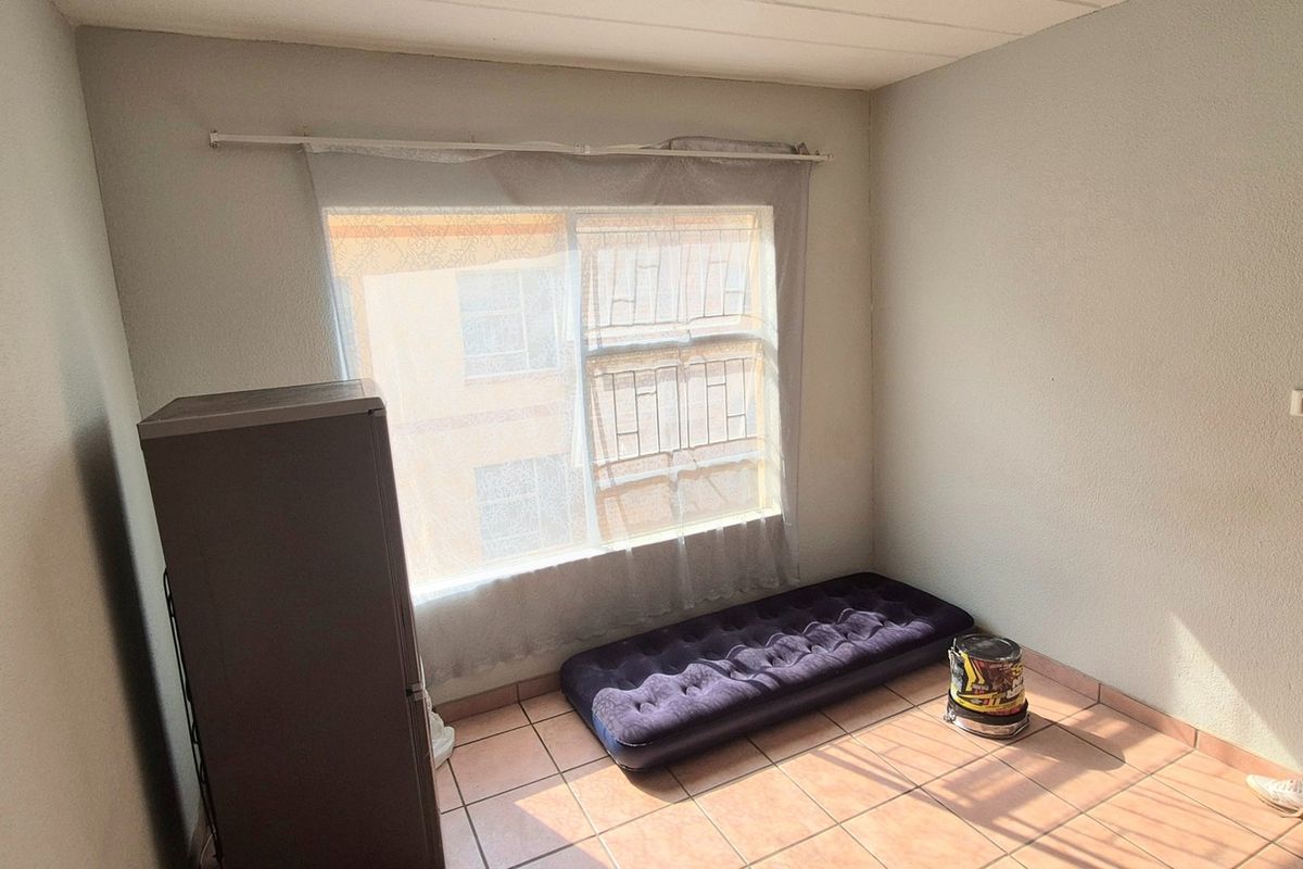 A simple bedroom featuring tiled flooring and a large window, providing a blank canvas for potential interior design and furnishing updates.