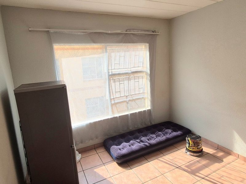 A simple bedroom featuring tiled flooring and a large window, providing a blank canvas for potential interior design and furnishing updates.