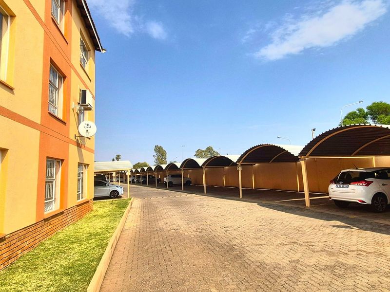 Exterior view of the apartment complex featuring a paved driveway and a row of covered parking bays.