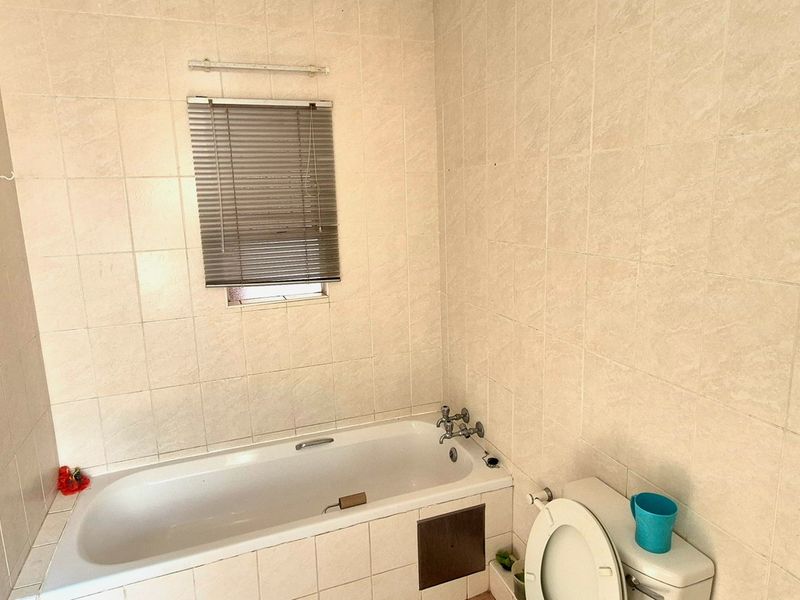 A functional bathroom featuring a bathtub, toilet, and full-height wall tiling, ready for cosmetic updates to modernize the space.