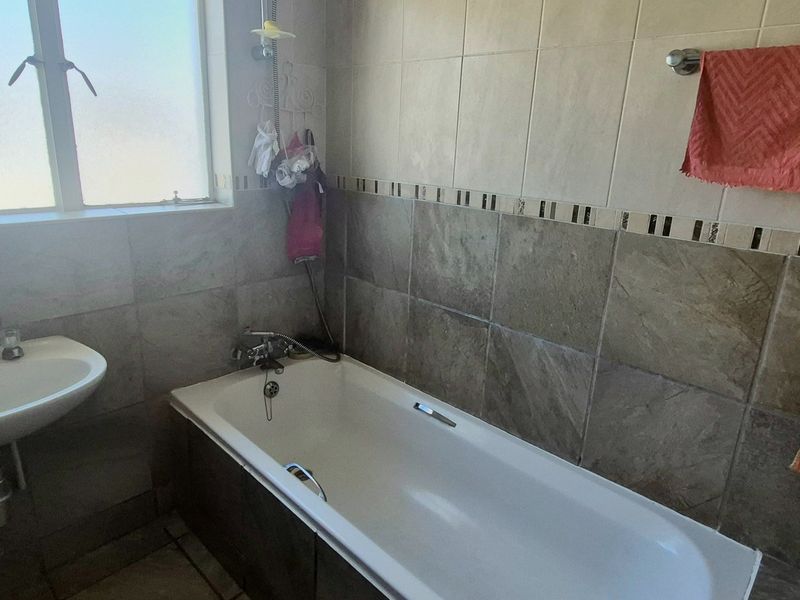 A functional bathroom featuring a bathtub, pedestal basin, and neutral wall tiling with a decorative border.