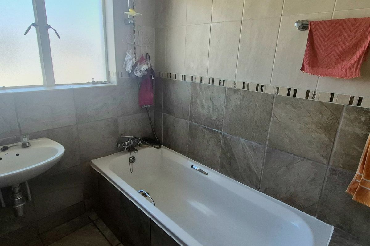 A functional bathroom featuring a bathtub, pedestal basin, and neutral wall tiling with a decorative border.