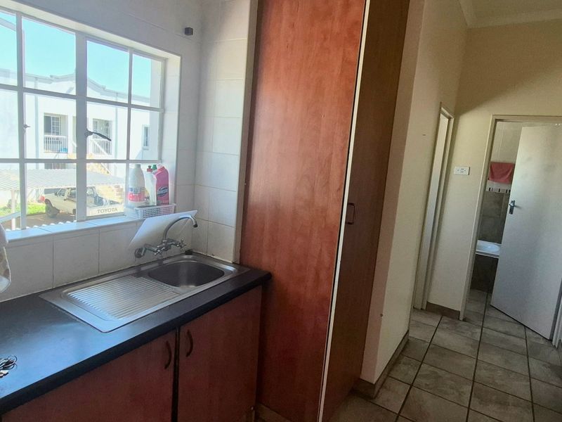 A functional scullery area featuring a stainless steel sink, laminate countertop, and built-in wooden cabinetry with tiled flooring.