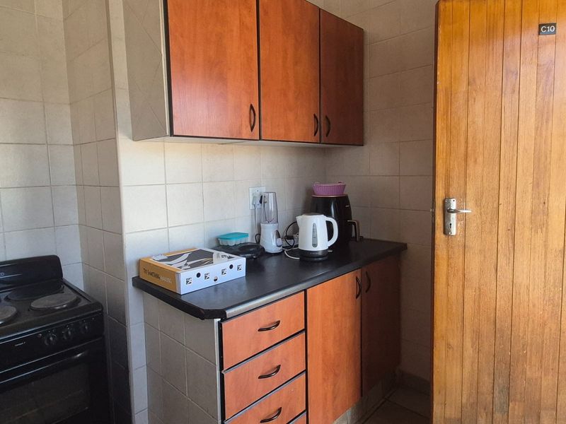 A compact kitchen featuring wooden cabinetry, a tiled splashback, and a freestanding electric stove, offering a functional layout with potential for modernization.