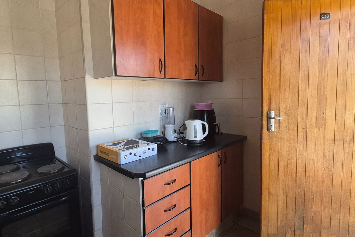 A compact kitchen featuring wooden cabinetry, a tiled splashback, and a freestanding electric stove, offering a functional layout with potential for modernization.