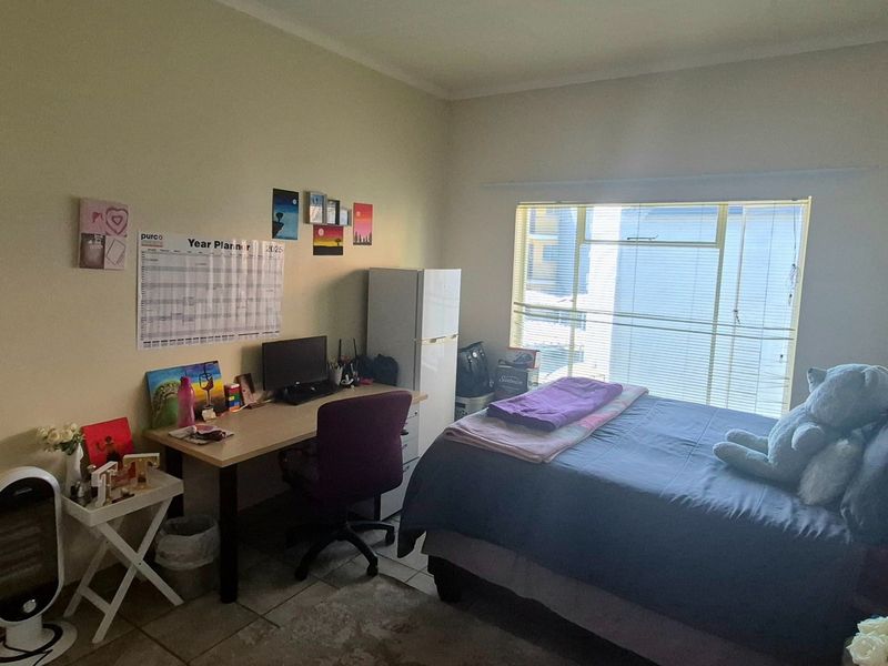 A functional bedroom featuring tiled flooring and a large window with horizontal blinds, providing natural light.
