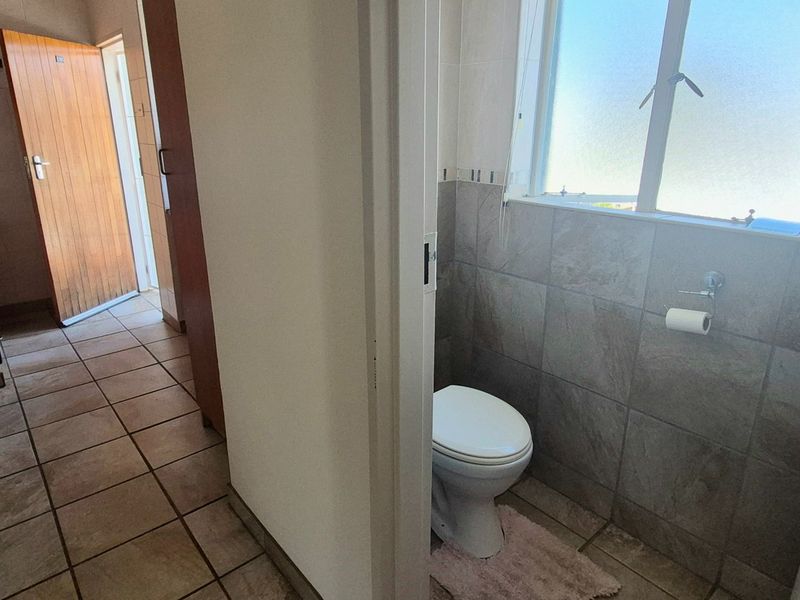 A functional bathroom featuring tiled walls, tiled flooring, and a frosted glass window, adjacent to a kitchen area.