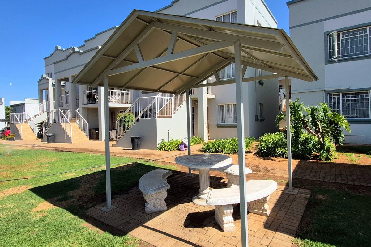 Communal outdoor area featuring a paved courtyard with a metal gazebo, landscaped garden, and access to apartment building staircases and balconies.