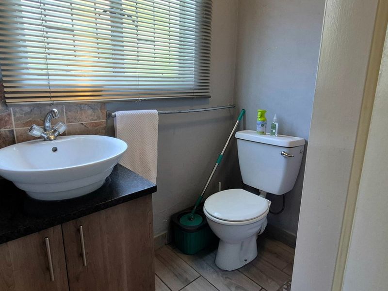 A compact bathroom featuring a vessel sink on a vanity cabinet, granite countertop, tiled backsplash, and a standard toilet with venetian blinds.