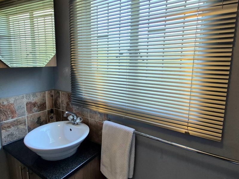 A functional bathroom featuring a vessel sink vanity, tiled splashback, medicine cabinet, and venetian blinds over the window.