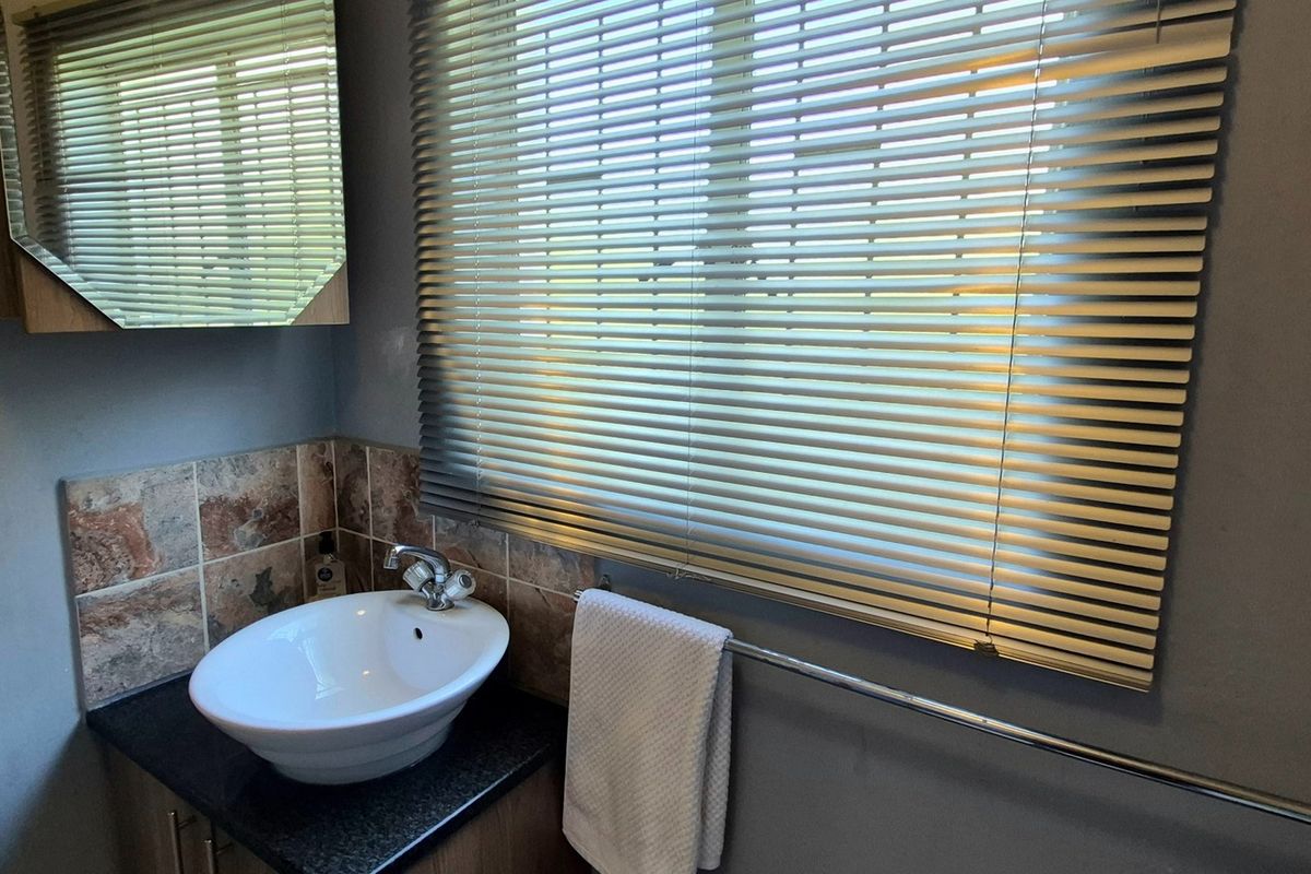 A functional bathroom featuring a vessel sink vanity, tiled splashback, medicine cabinet, and venetian blinds over the window.