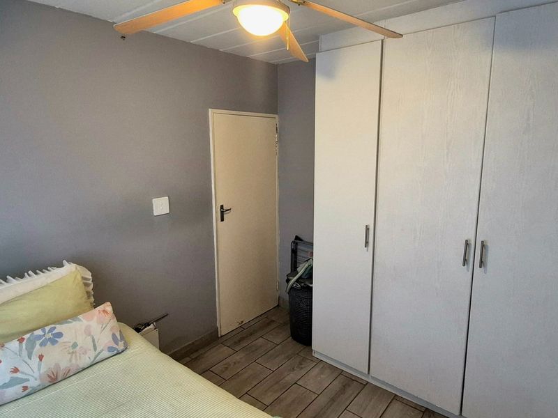 A bedroom featuring built-in cupboards, a ceiling fan, and tiled flooring, providing a functional and neutral living space.