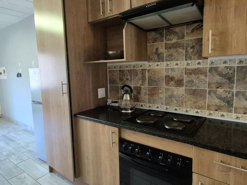 A functional kitchen featuring wood-look cabinetry, dark laminate countertops, a built-in electric oven and hob, and a decorative tiled backsplash.