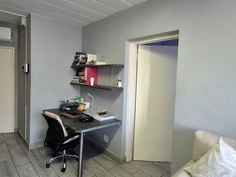 Open plan living area featuring tiled flooring, a built-in desk with floating shelving, and an integrated air conditioning unit.