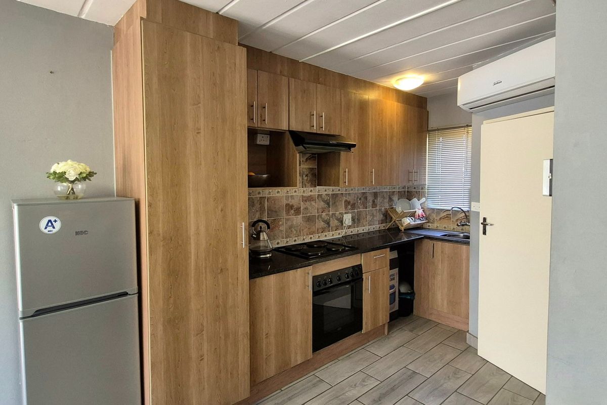 A compact, functional kitchen featuring wood-look cabinetry, dark countertops, built-in oven and hob, tiled backsplash, and an integrated air conditioning unit.