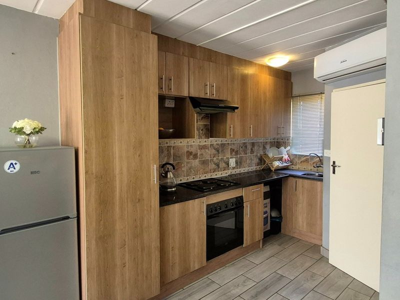 A compact, functional kitchen featuring wood-look cabinetry, dark countertops, built-in oven and hob, tiled backsplash, and an integrated air conditioning unit.