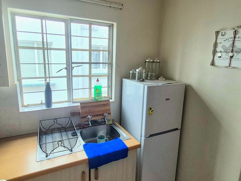 A compact kitchen area featuring a stainless steel sink, laminate countertops, and built-in cabinetry with security bars on the window.