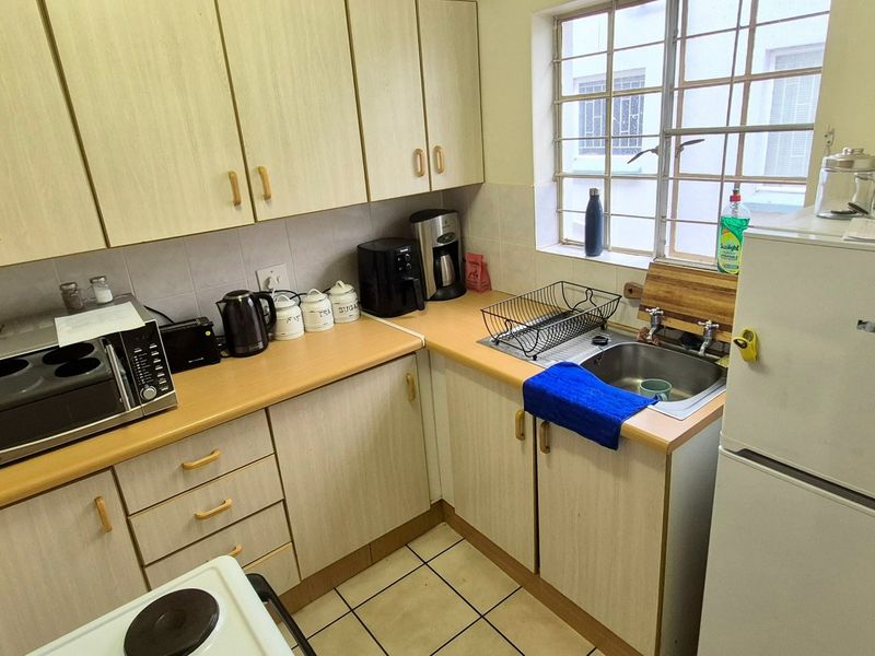 Compact kitchen featuring laminate cabinetry, tiled flooring, and a stainless steel sink with a window providing natural light.
