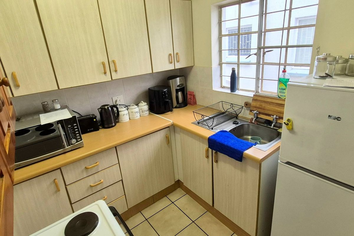 Compact kitchen featuring laminate cabinetry, tiled flooring, and a stainless steel sink with a window providing natural light.