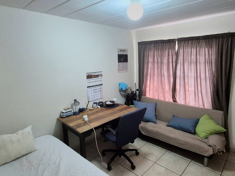 A functional bedroom featuring tiled flooring, a built-in wall cabinet, and a timber door, providing a practical space for rest or study.