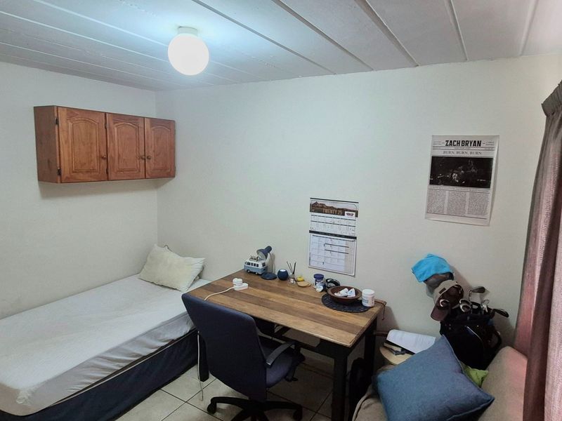 A compact bedroom featuring tiled flooring, wall-mounted storage cabinetry, and neutral wall finishes, suitable for a guest room or home office.